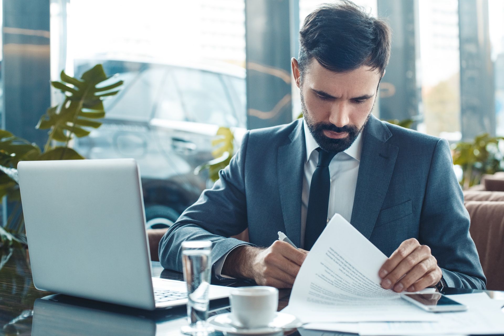 Un hombre con traje y corbata está sentado en una mesa con una computadora portátil y una taza de café.