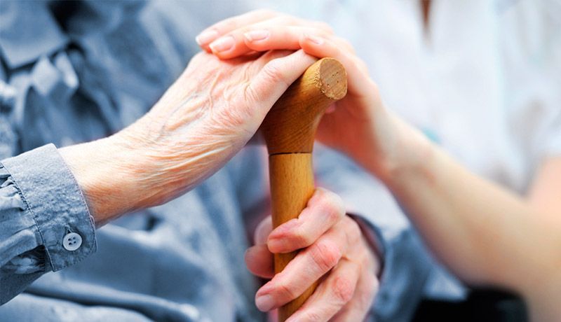 Una mujer sostiene la mano de una anciana mientras sostiene un bastón.