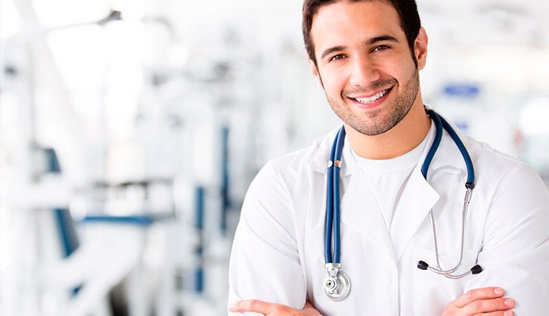 Un médico sonriente con un estetoscopio alrededor del cuello está de pie en un hospital con los brazos cruzados.