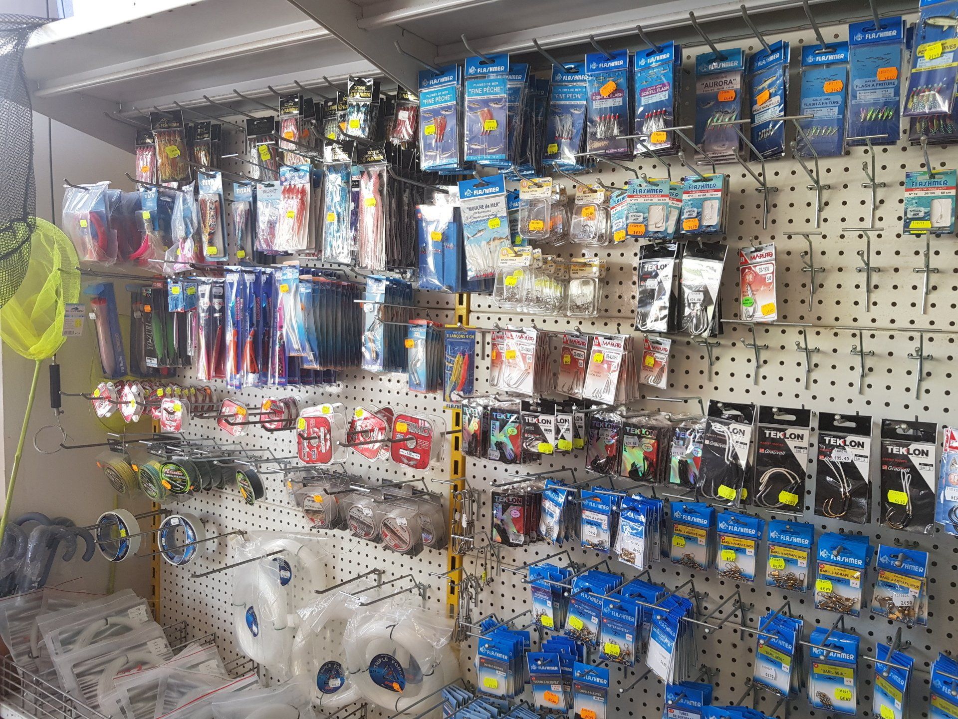 Présentoir d'articles de pêche dans un magasin, comprenant divers leurres, hameçons et équipements sur un panneau perforé.
