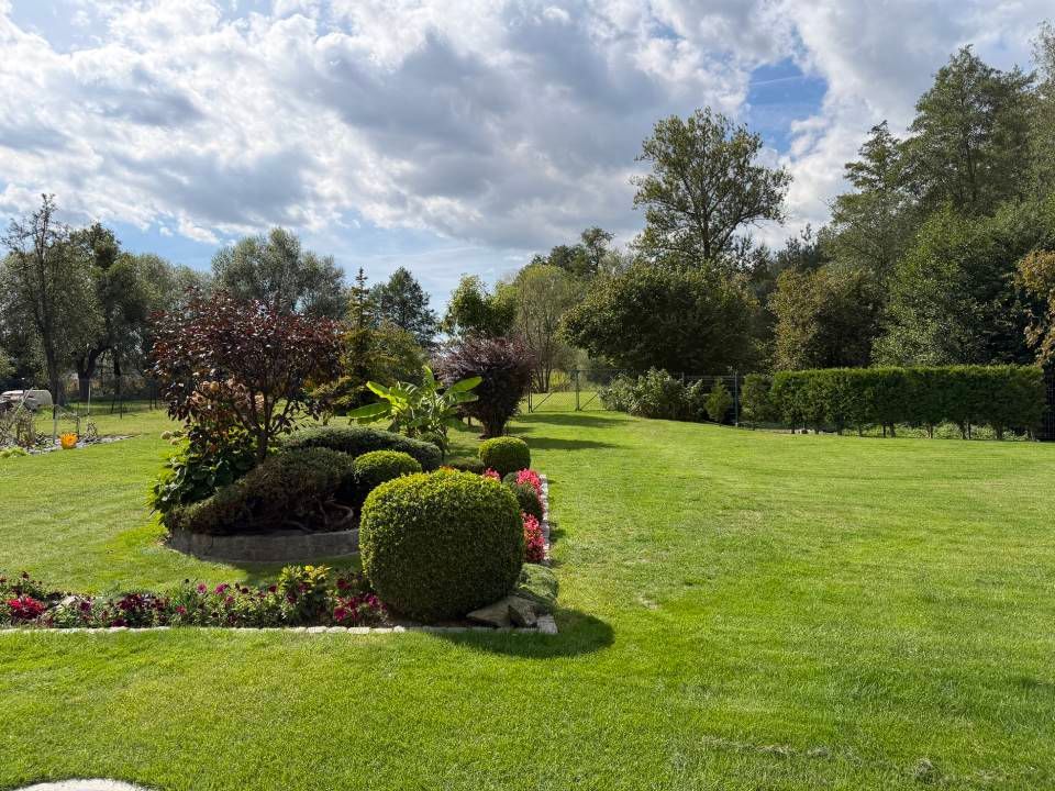 Üppiger Garten mit gestutzten Sträuchern, Blumenbeeten und einer weitläufigen grünen Rasenfläche unter bewölktem Himmel