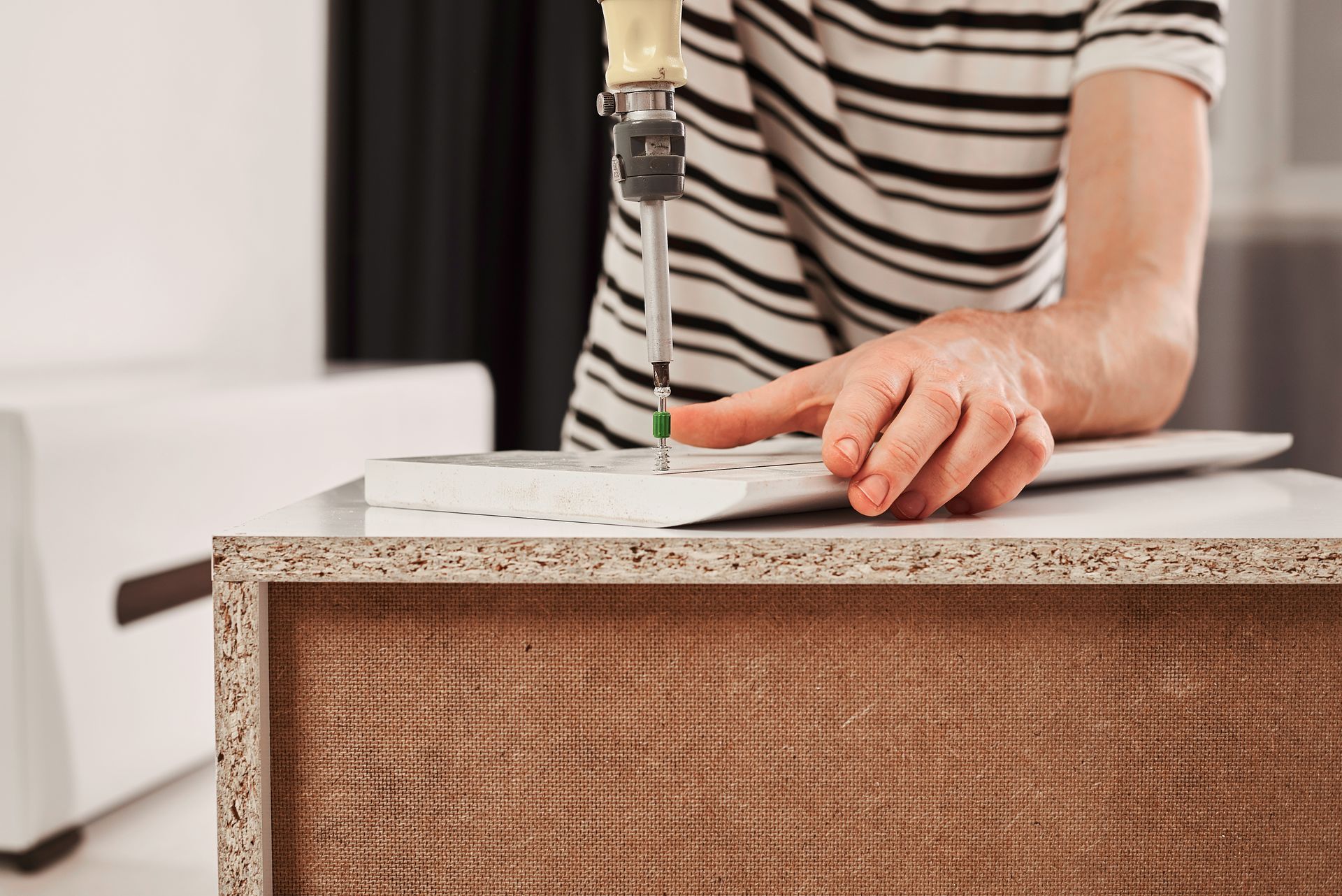 Une personne portant une chemise à rayures utilise un tournevis pour assembler des meubles en bois blanc.