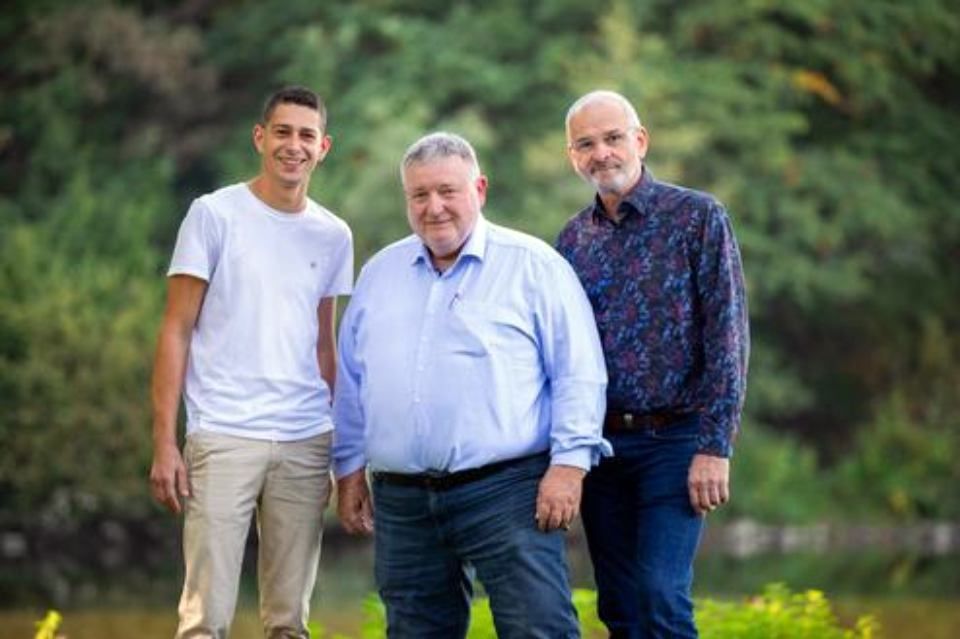 Drei Männer stehen nebeneinander in einem Park.