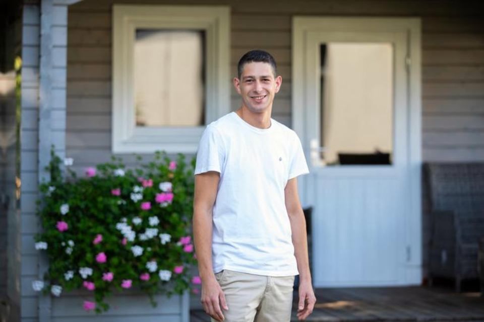 Ein Mann in einem weißen Hemd und Khakihosen steht vor einem Haus.