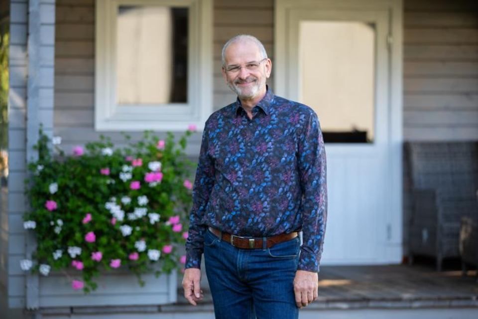 Ein Mann steht auf der Veranda eines Hauses mit Blumen im Hintergrund.