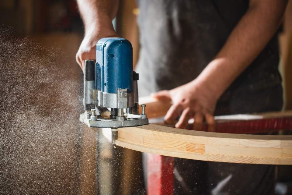 Ein Mann schneidet mit einer Oberfräse ein Stück Holz.