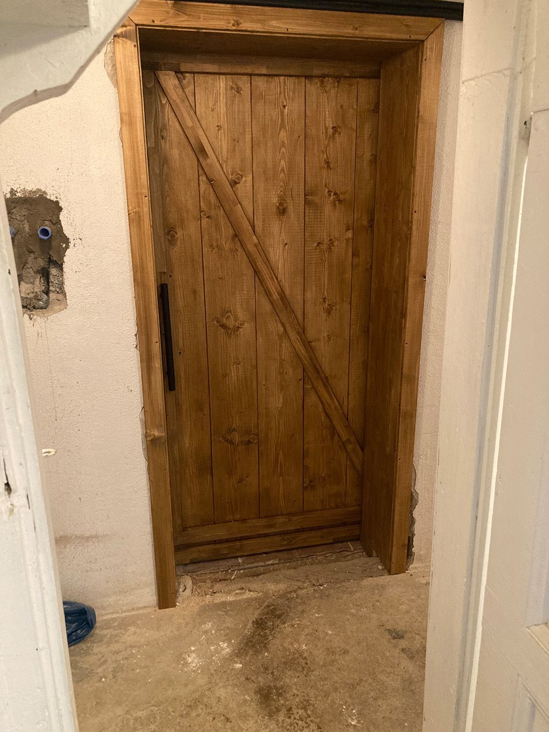 In einem Raum neben einer weißen Wand befindet sich eine Holztür.