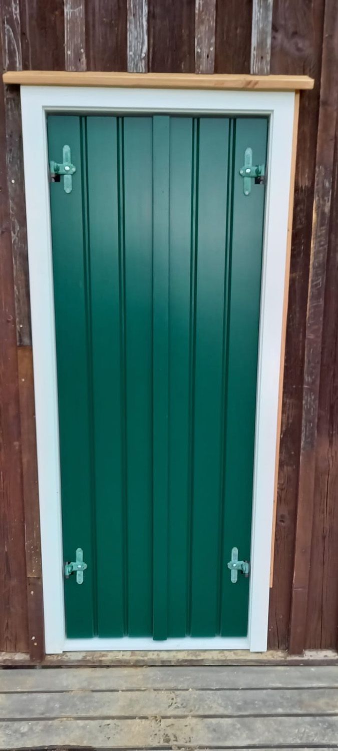An einer Holzwand befindet sich eine grüne Tür mit weißen Fensterläden.
