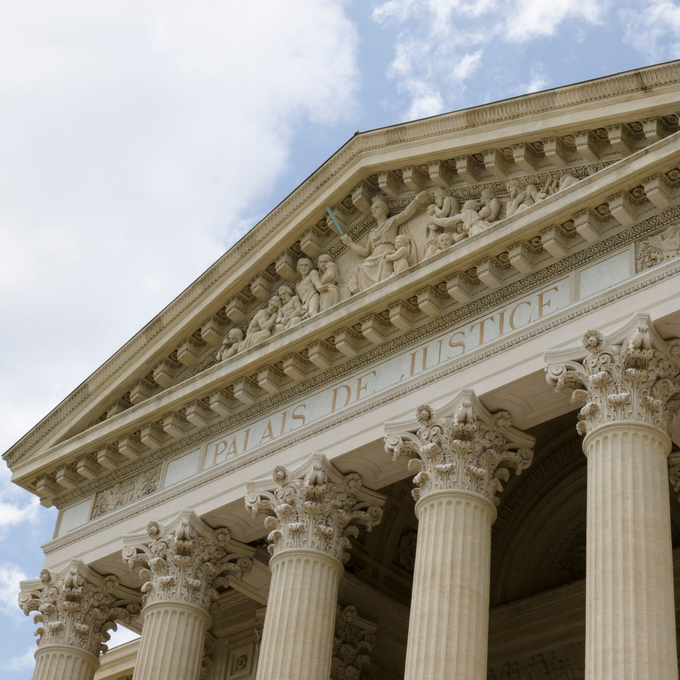 Façade classique d'un palais de justice avec de hautes colonnes corinthiennes et un fronton orné se détachant sur un ciel bleu