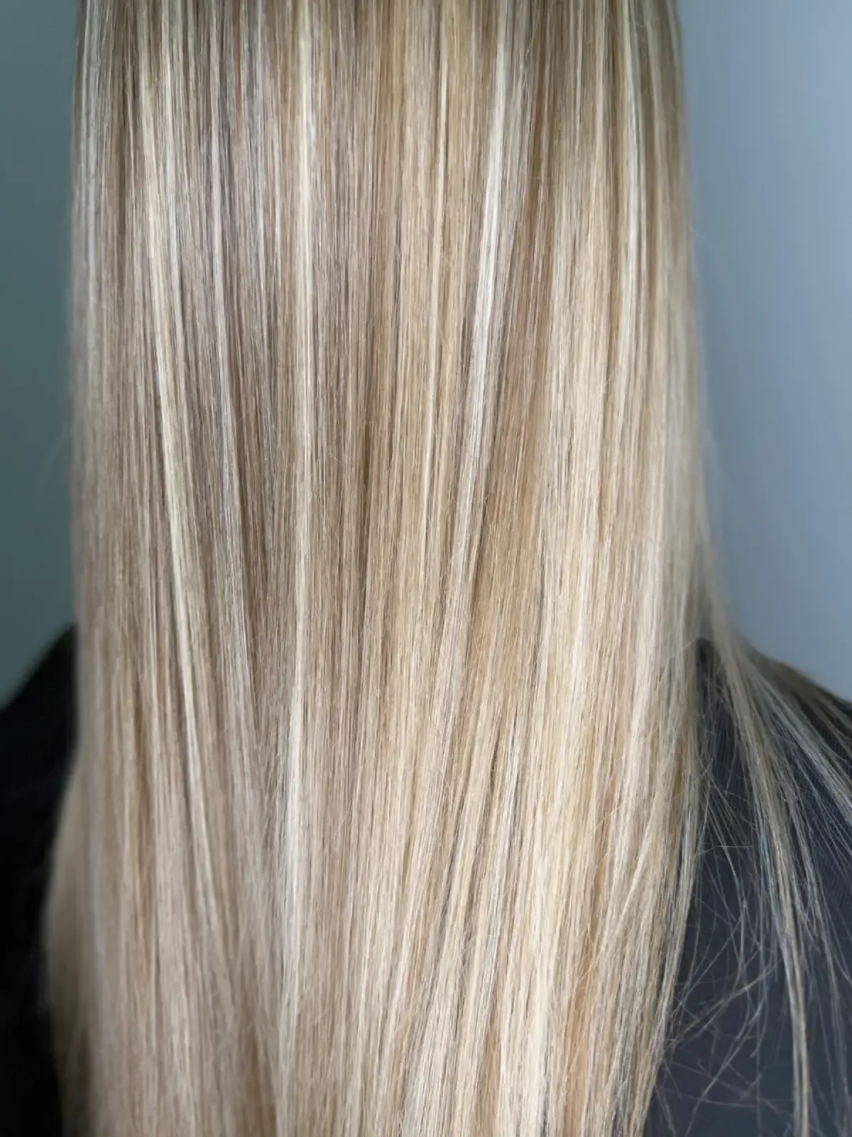 Primer plano de una larga melena rubia lisa con sutiles reflejos sobre un fondo gris.