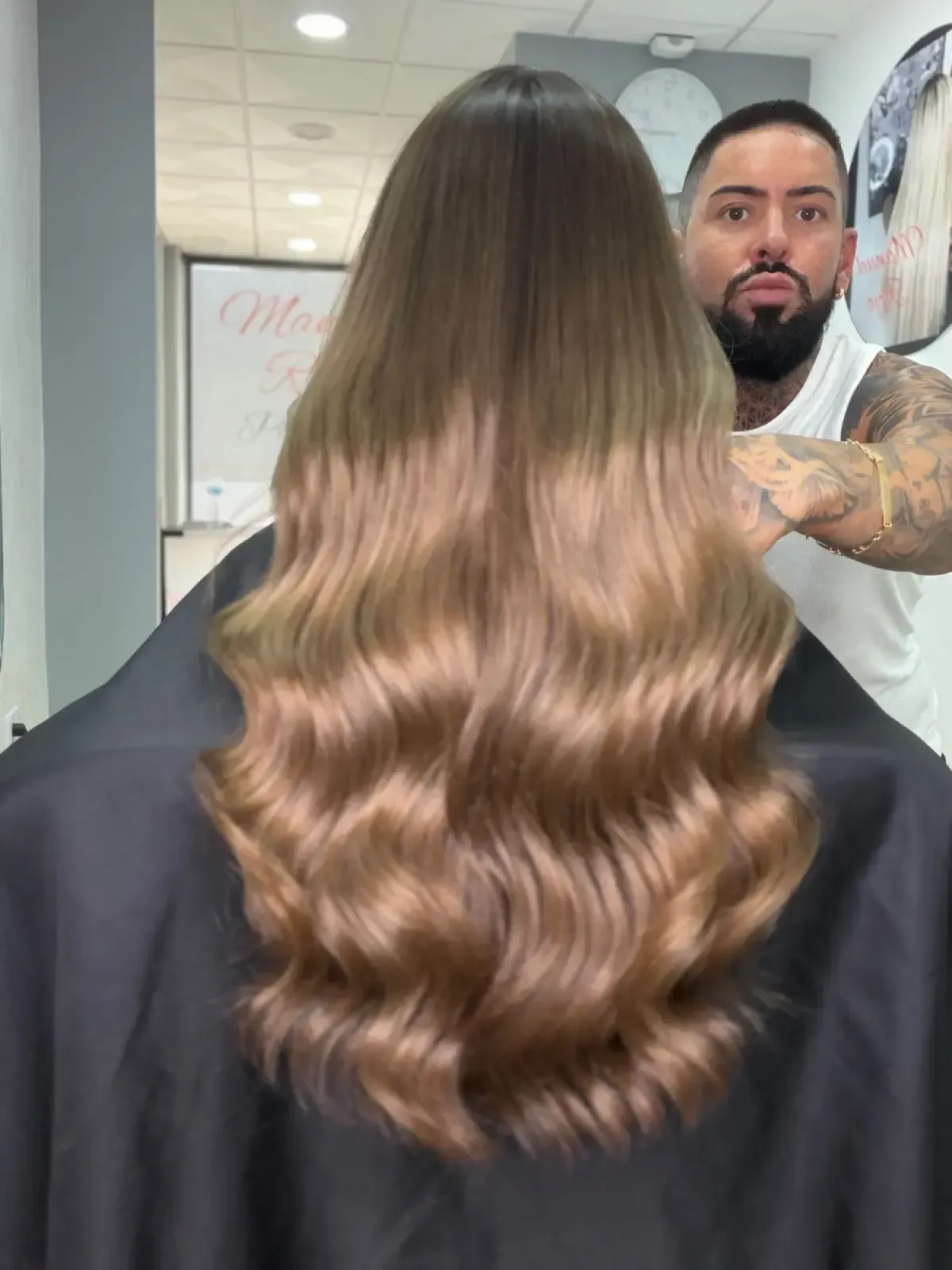 Cabello largo y ondulado castaño peinado en una peluquería, con un estilista al fondo.