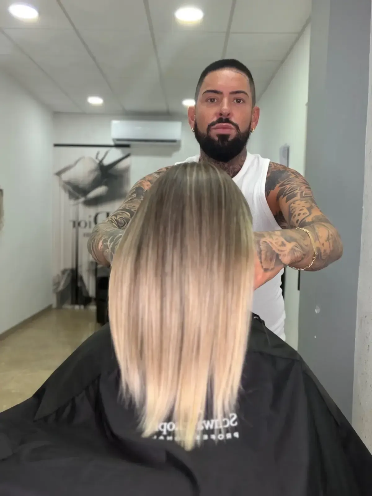 Peluquera trabajando en un corte de pelo bob rubio en un salón con paredes blancas y luces de techo.