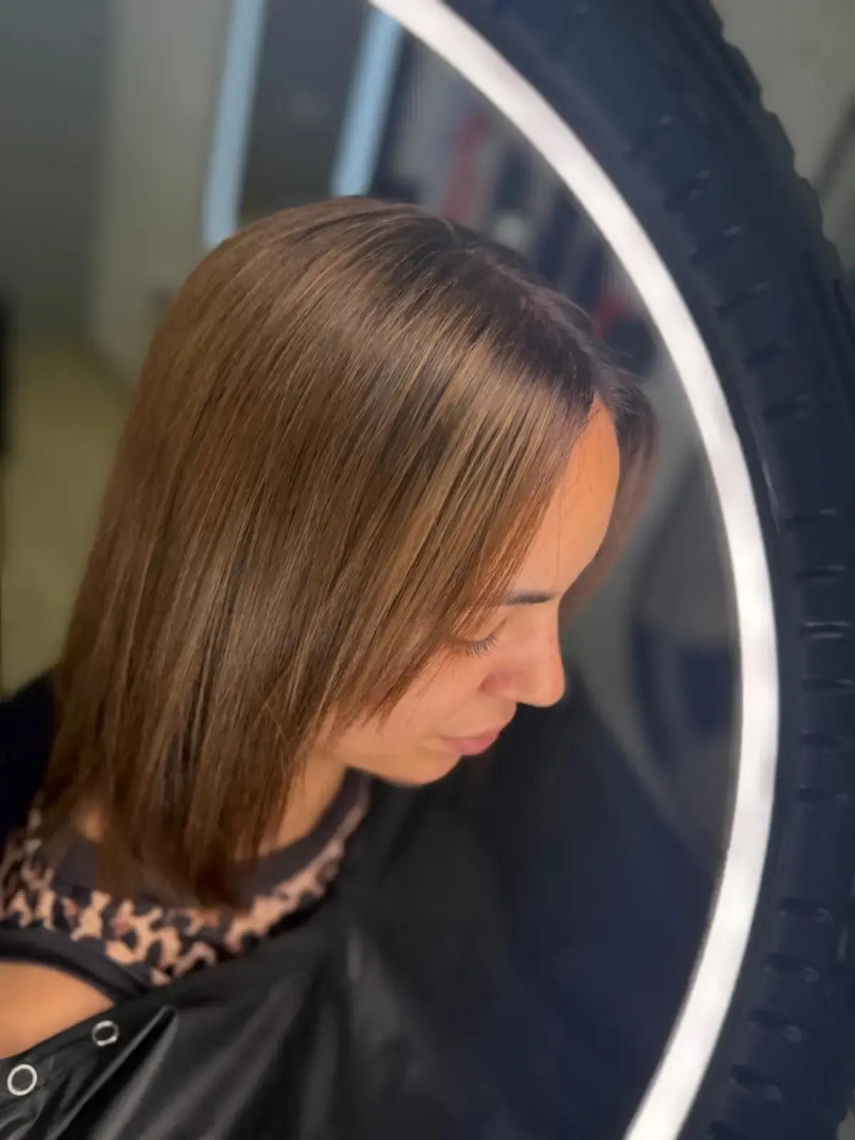 Mujer con cabello castaño liso mirando hacia abajo cerca de un anillo de luz encendido