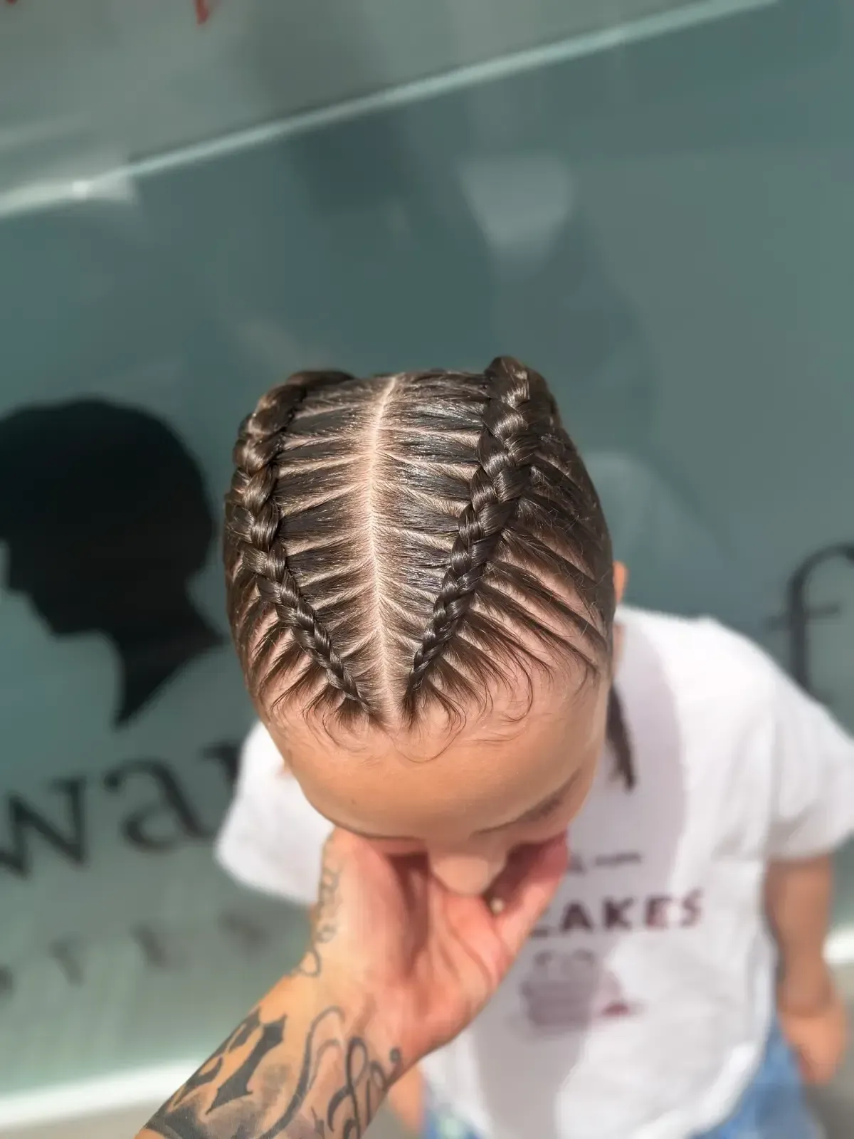 Vista superior de una persona con trenzas africanas, mirando hacia abajo, con una camisa blanca al aire libre.