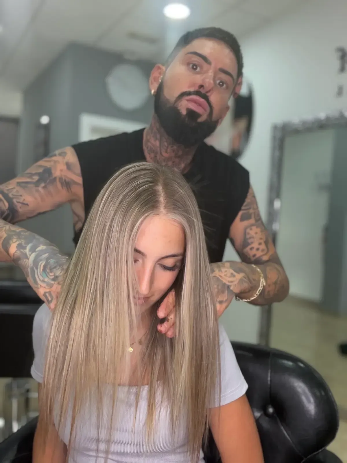 Una estilista le hace una trenza a una clienta con su larga melena rubia sentada en una silla de peluquería.