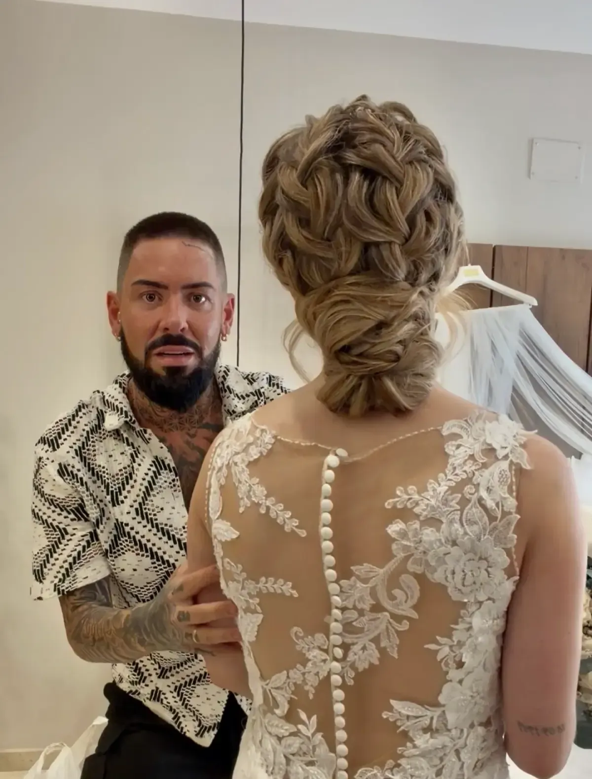 La novia, con un vestido de encaje en la espalda, mira al hombre en el interior de la casa