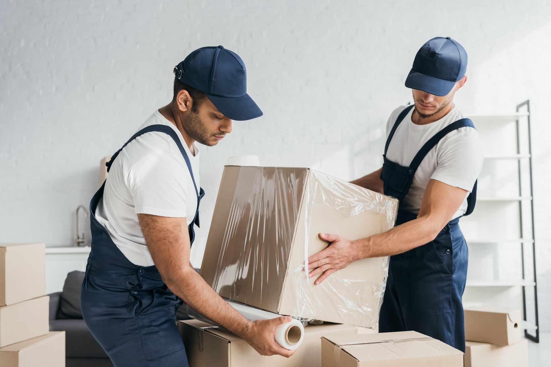 Deux déménageurs emballent un grand carton avec du film plastique.