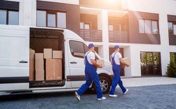 Deux déménageurs en uniforme déchargent des cartons d'une camionnette devant un immeuble.