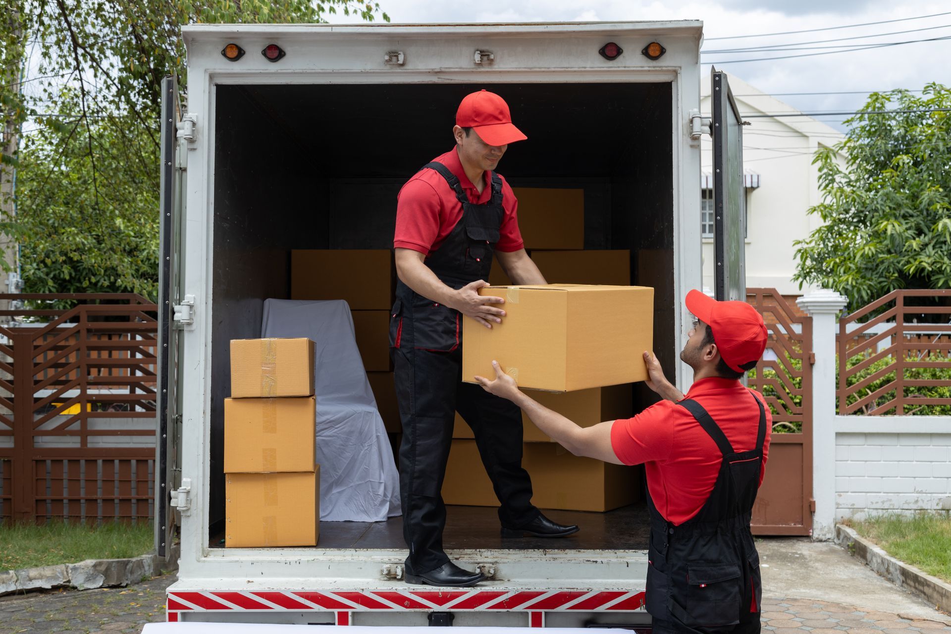 Deux déménageurs en uniforme chargent des cartons dans un camion de déménagement à l'extérieur.