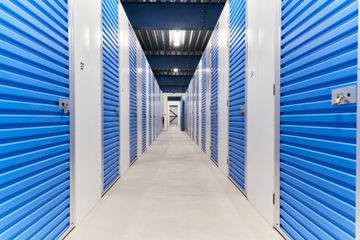 Couloir étroit bordé de portes de box de stockage, sol en béton et éclairage au plafond.