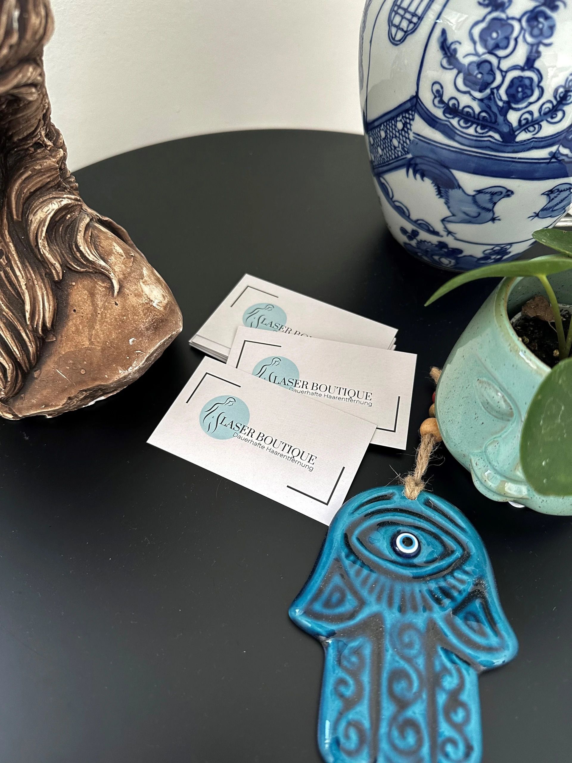 Eine Hamsa-Hand liegt auf einem Tisch neben einer Vase und einer Pflanze.