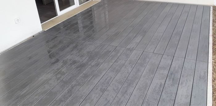 Revêtement de terrasse imitation bois gris près de l’entrée d’un bâtiment blanc