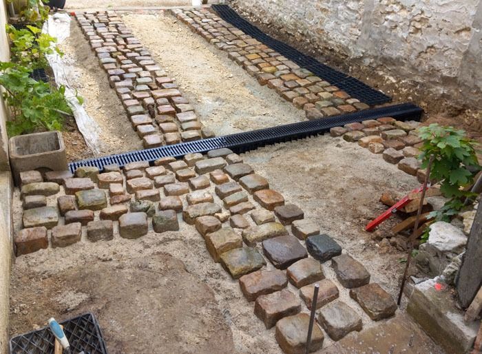 Allée en pierre et en briques en cours de construction le long d’un mur en pierre, avec des outils.