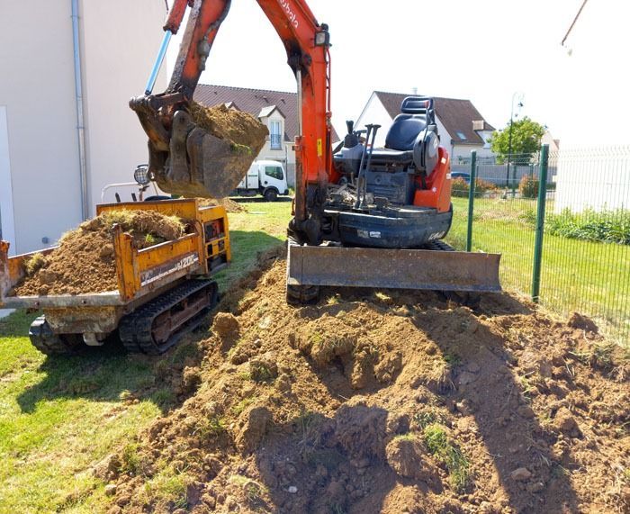 Une pelleteuse et un camion-benne déplacent de la terre sur un chantier à côté d’une maison.