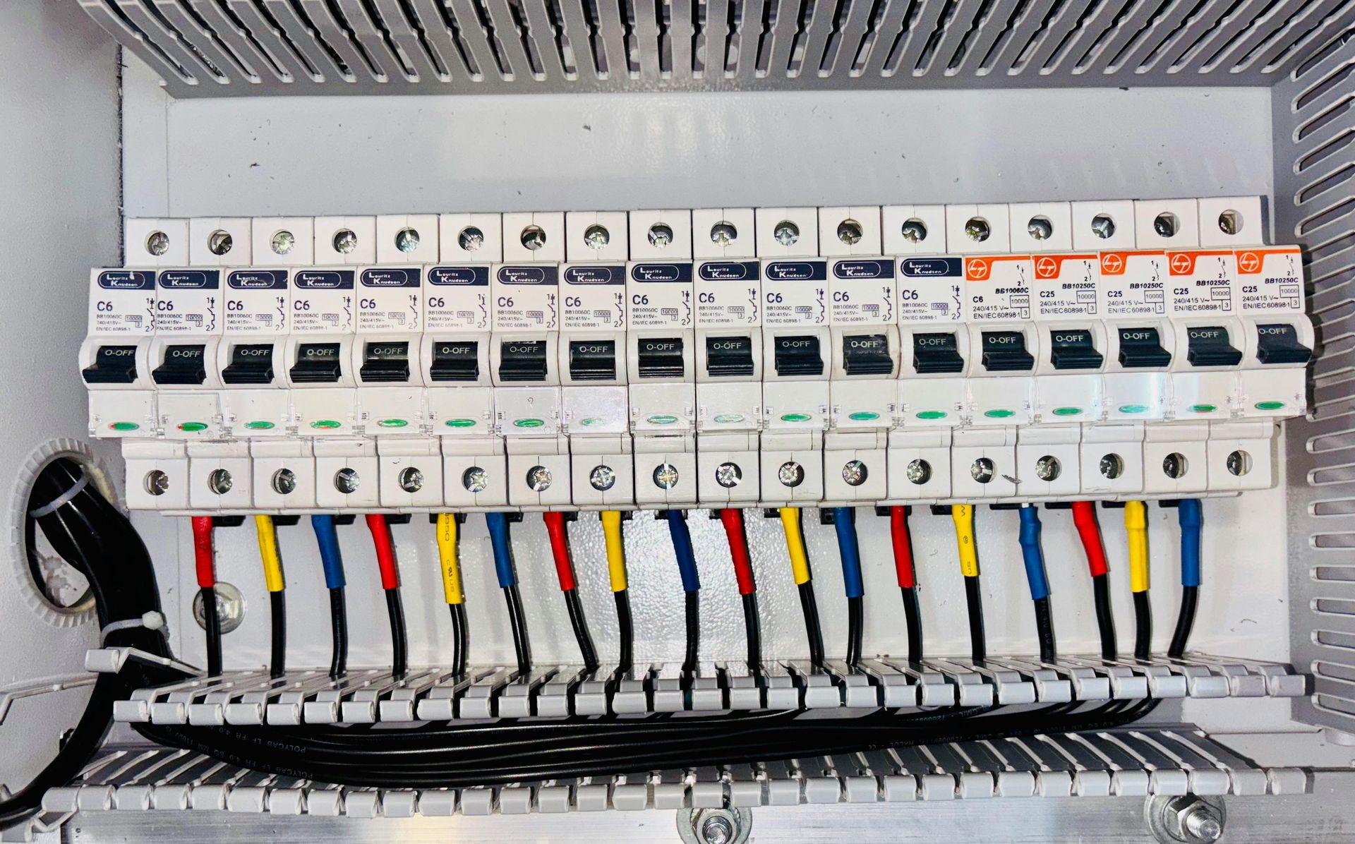Una fila de disyuntores en un gabinete eléctrico de metal, con cables codificados por colores
