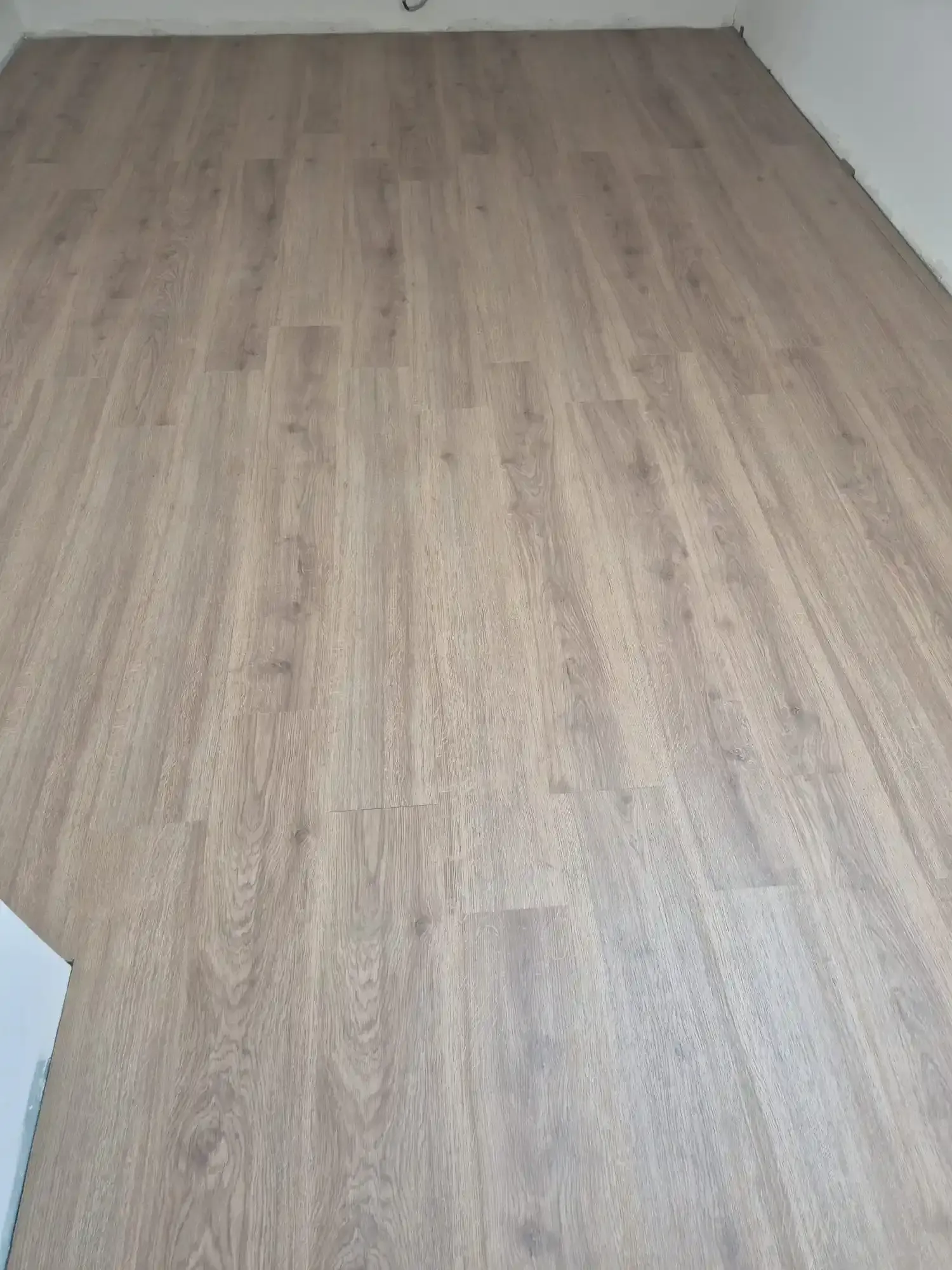 Habitación vacía con suelo de madera clara y paredes blancas, vista desde una esquina.