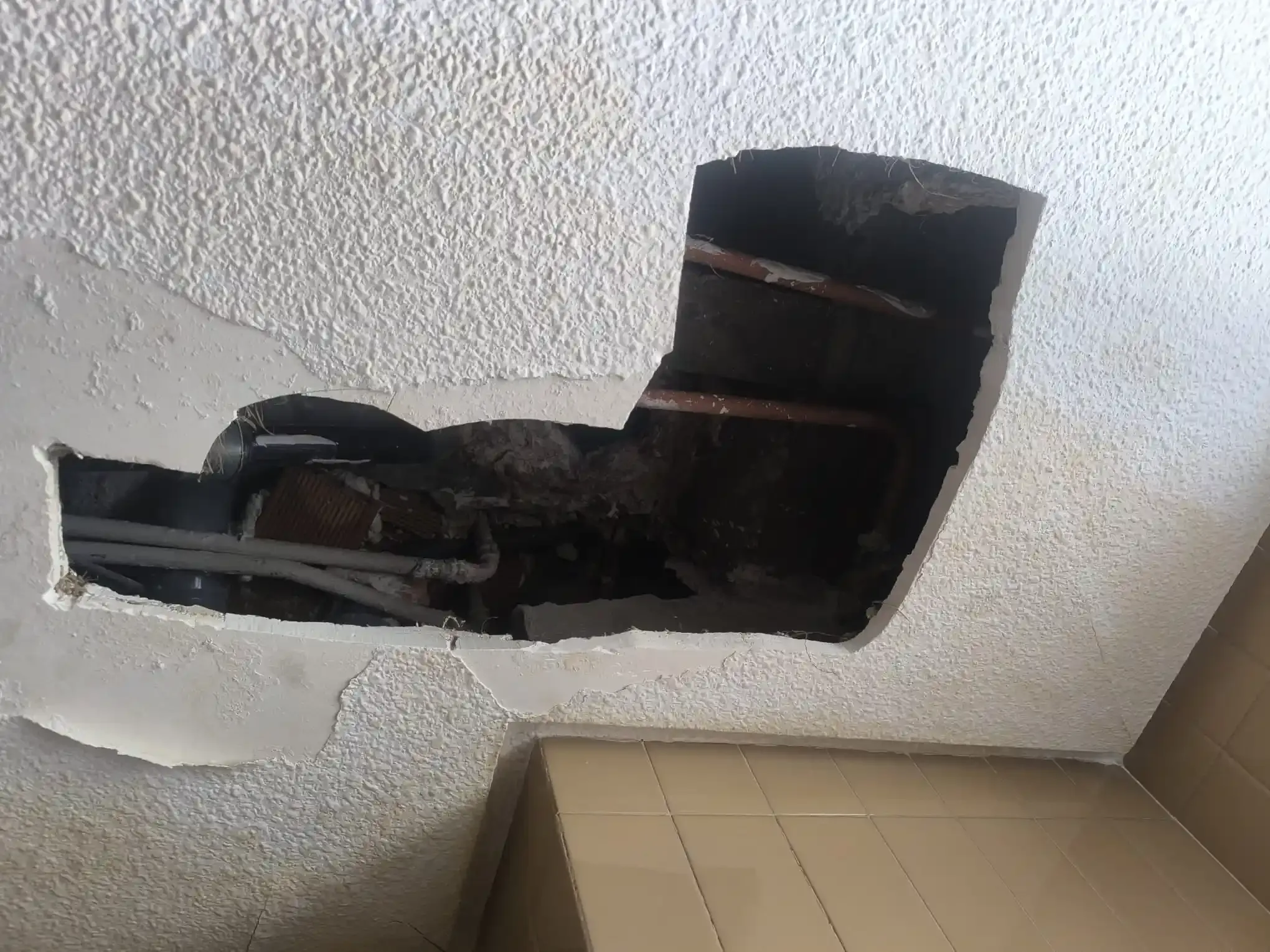 Techo dañado con un gran agujero que deja al descubierto la estructura interior oscura y el panel aislante cercano.
