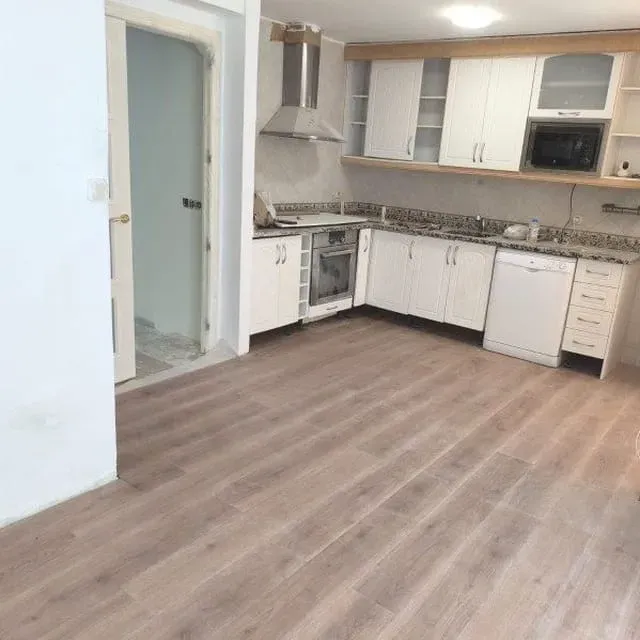 Cocina moderna vacía con gabinetes blancos, encimeras de granito y piso de madera clara.