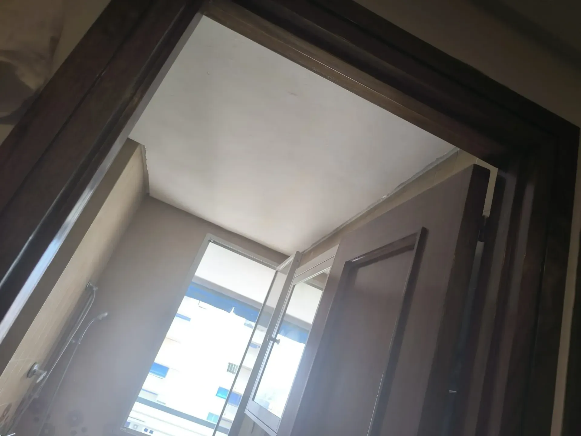 Puerta de madera abierta con luz natural brillante que entra por una ventana al otro lado.