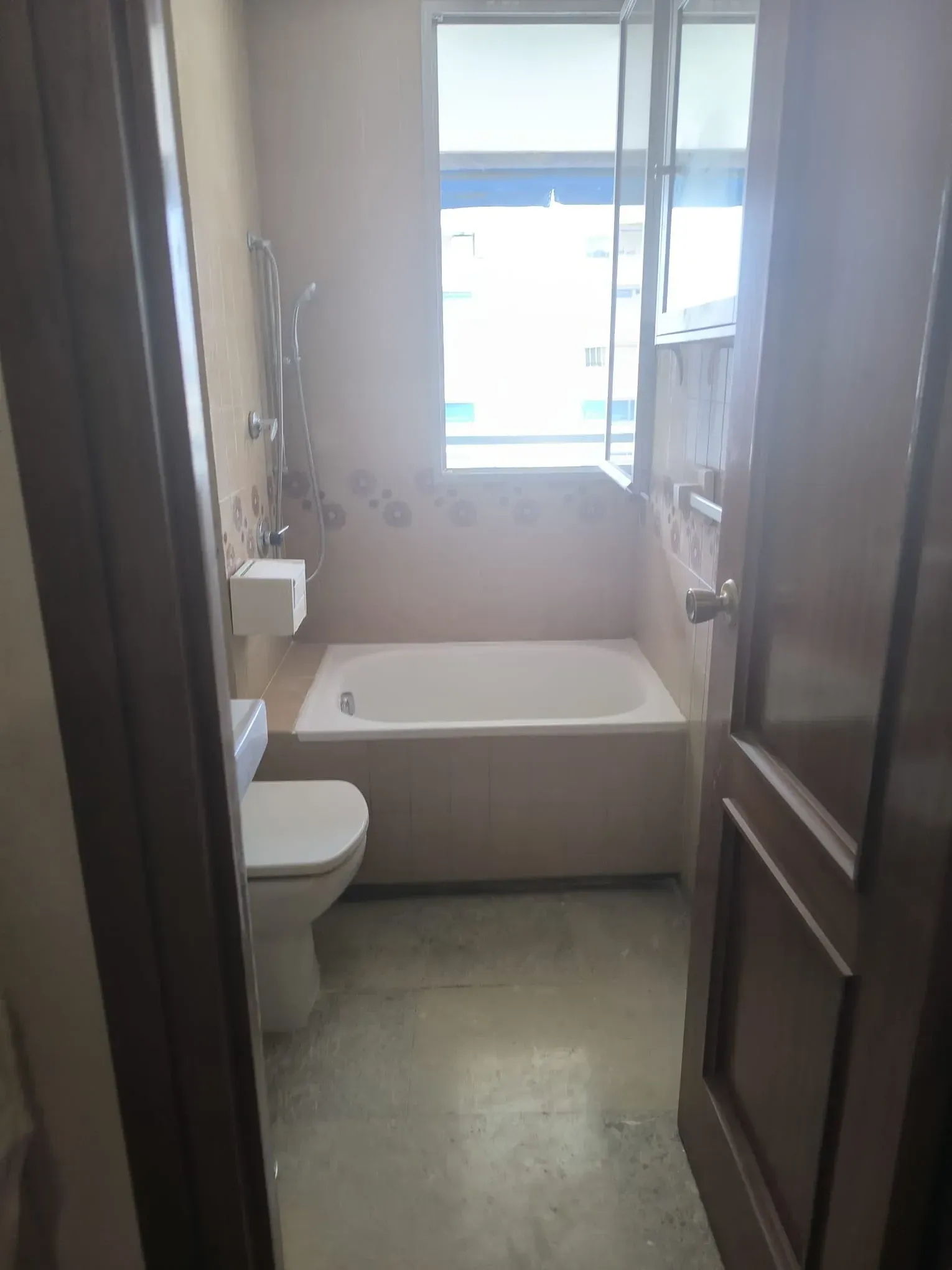 Baño estrecho con inodoro, bañera y ventana, visto desde la puerta.