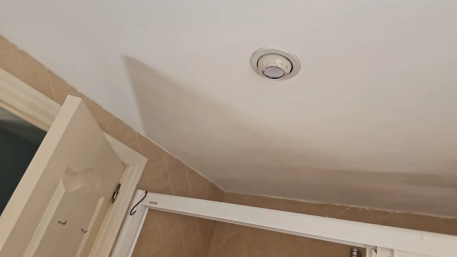 Techo del baño con un detector de humo redondo sobre una puerta abierta y un armario.