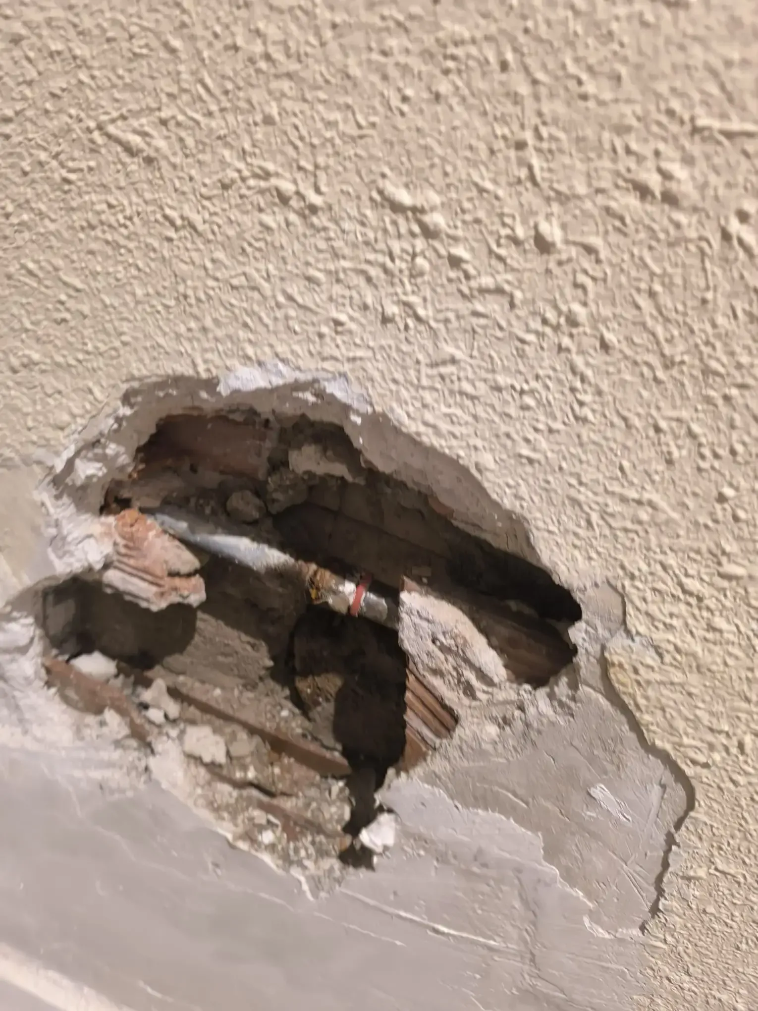 Agujero en una pared beige que deja al descubierto el yeso dañado y el cableado.