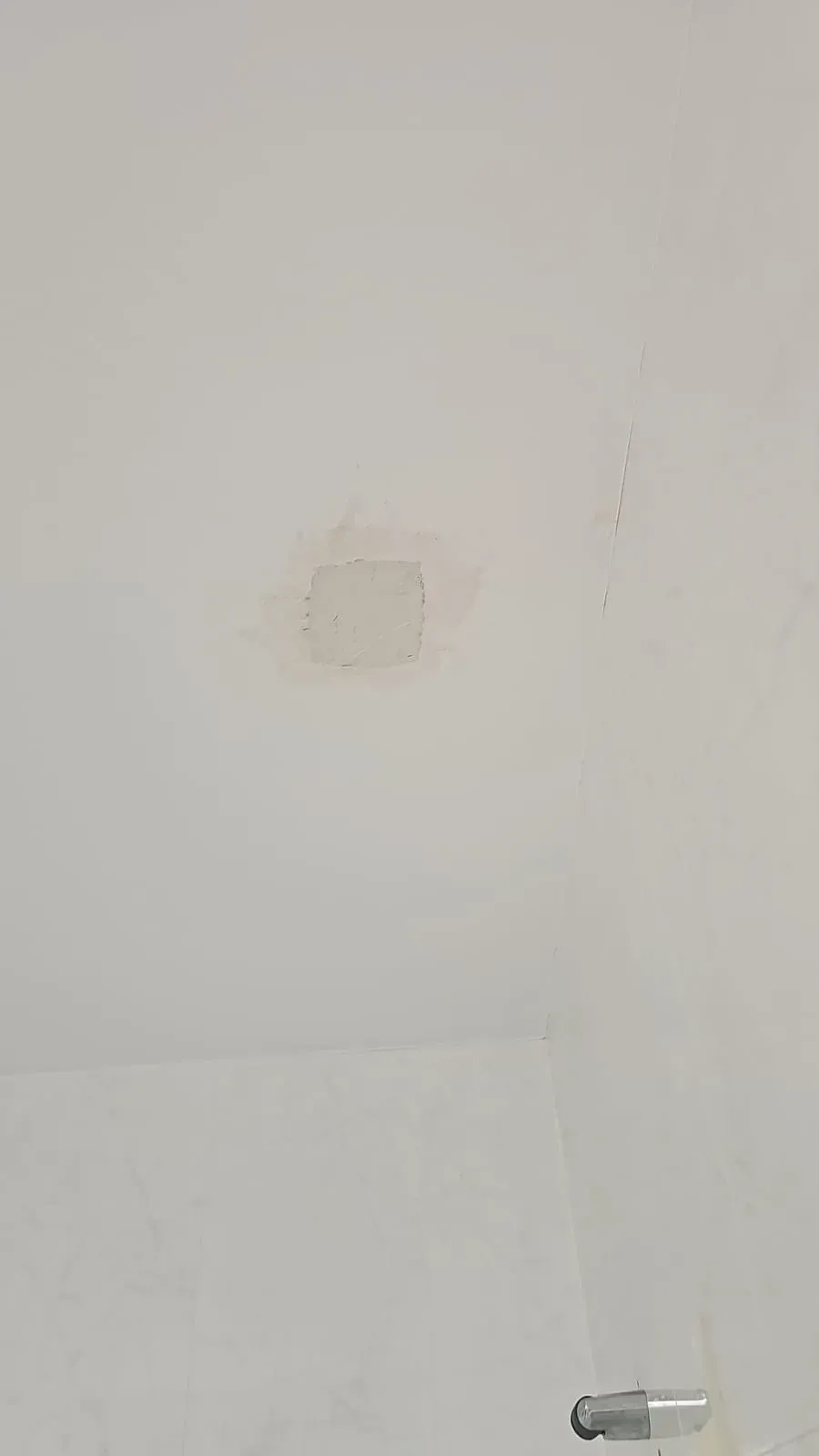 Pared blanca con una pequeña zona desgastada cerca del centro y un accesorio metálico en la parte inferior derecha.