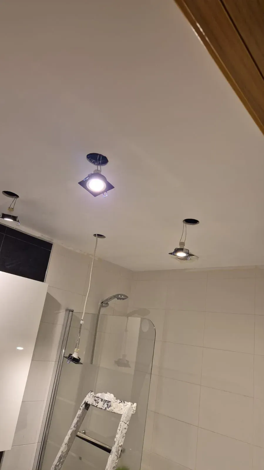 Ducha de baño con paredes de azulejos blancos, puerta de cristal y luces de techo en un techo inclinado.