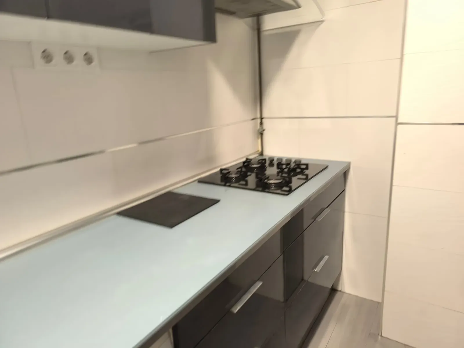 Encimera de cocina moderna con placa de cocina negra, fregadero y paredes alicatadas en blanco.