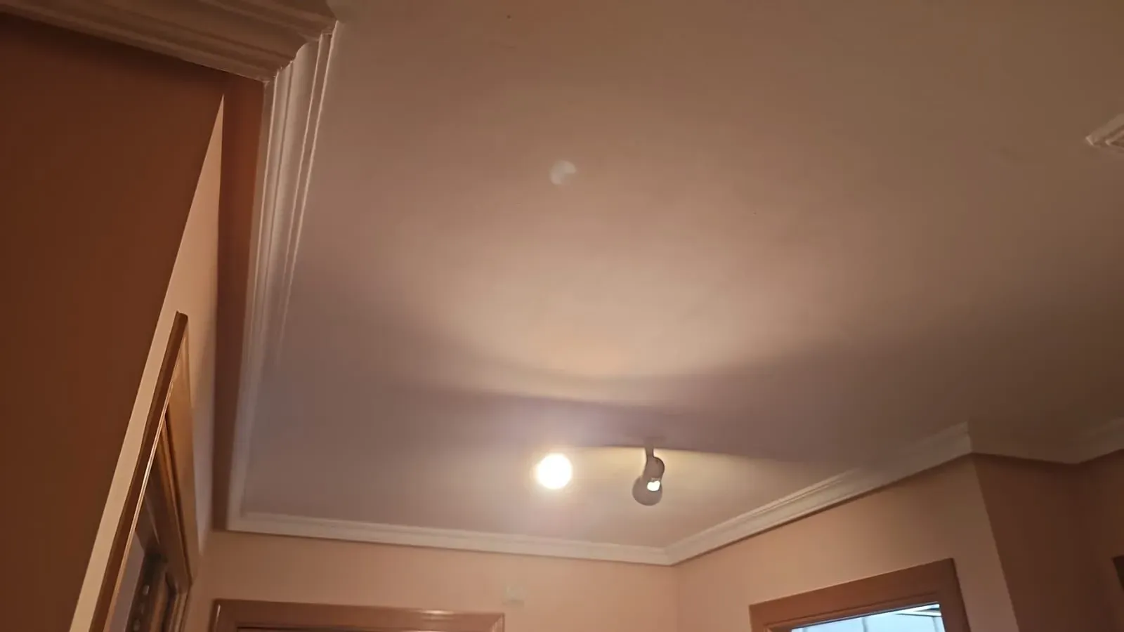 Esquina del techo con moldura decorativa, una bombilla encendida