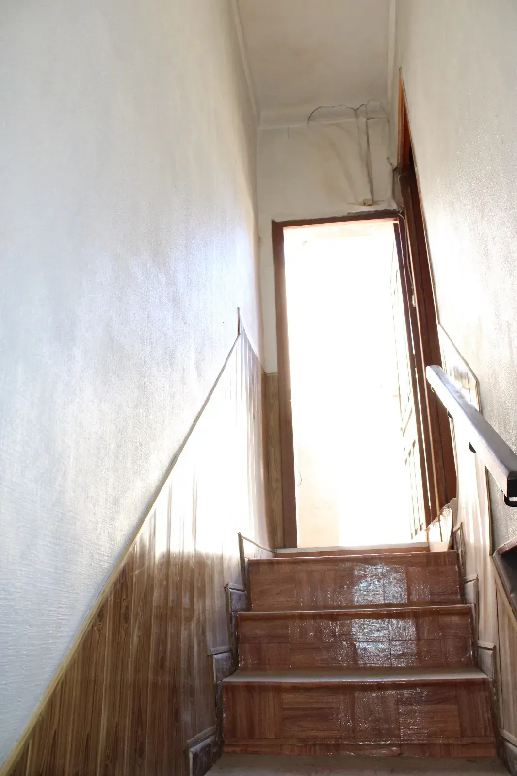 Una estrecha escalera con escalones de madera conduce a una puerta luminosa en la parte superior.