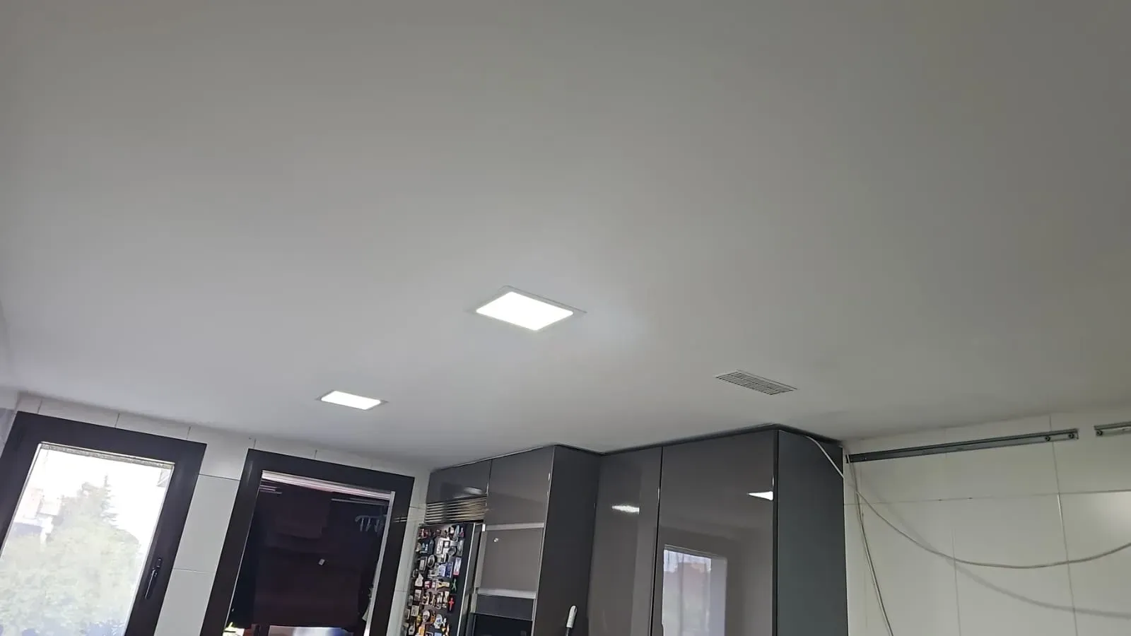 Habitación interior con luces blancas en el techo, paredes grises, ventanas y armarios cerca de una puerta.