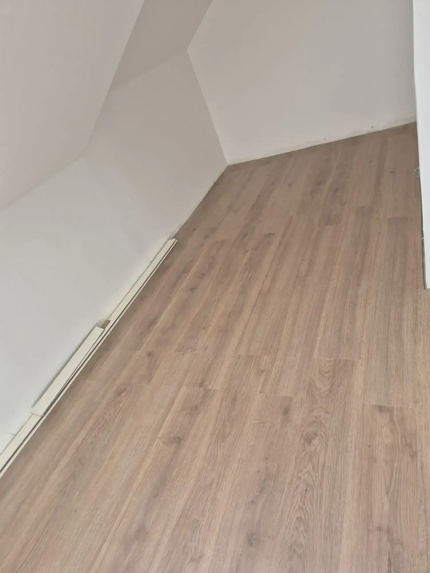 Habitación vacía en el ático con paredes blancas y suelo de madera clara