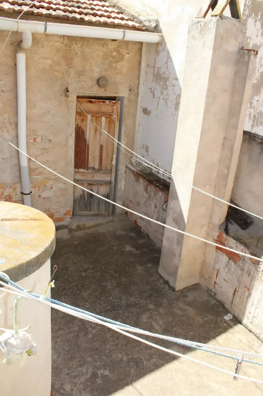 Pequeño patio con una puerta de madera desgastada, paredes de color beige y tendederos colgados en el techo.
