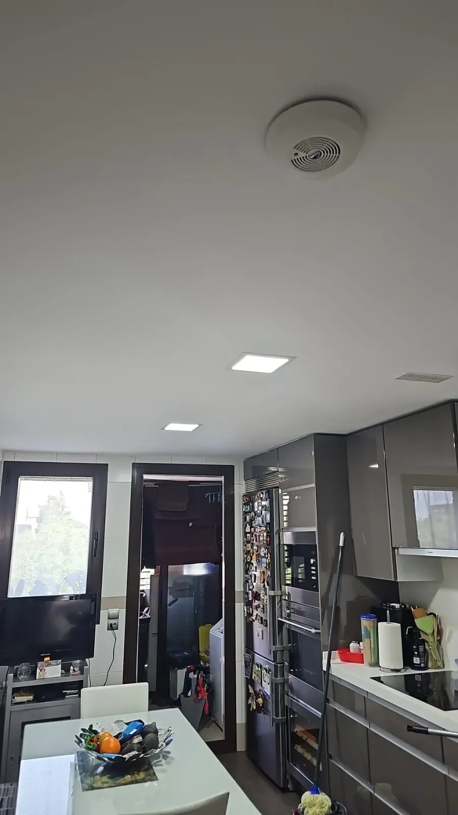 Cocina moderna y luminosa con luces blancas en el techo, armarios grises y una puerta con ventana en la parte trasera.