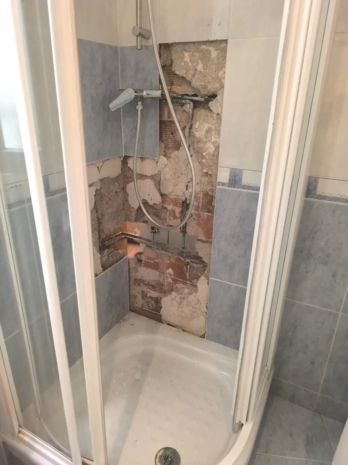 Pared de la ducha dañada, con tuberías expuestas y yeso roto encima de la bañera.