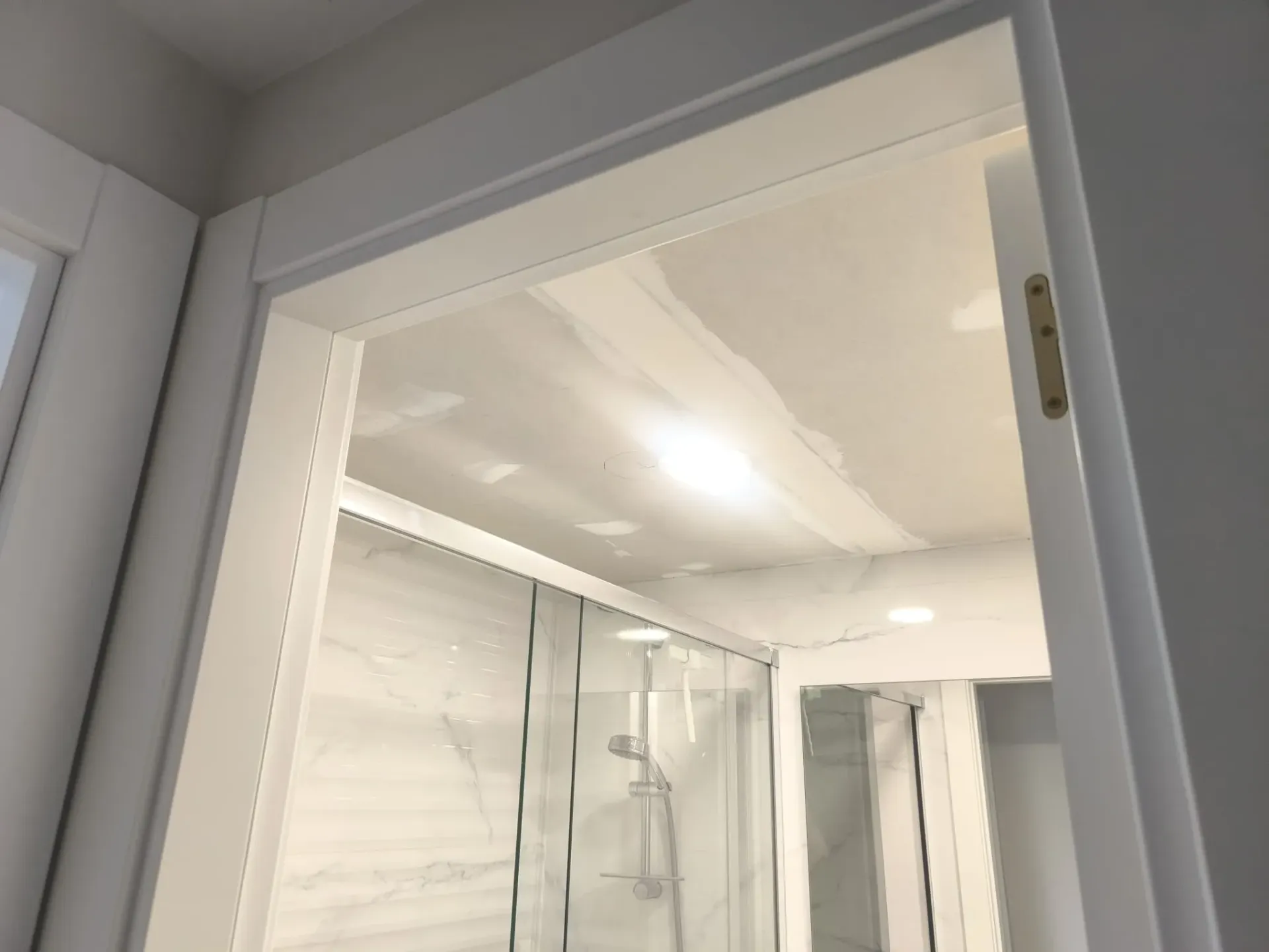 Entrada abierta a un luminoso baño blanco con ducha de cristal y paredes alicatadas.