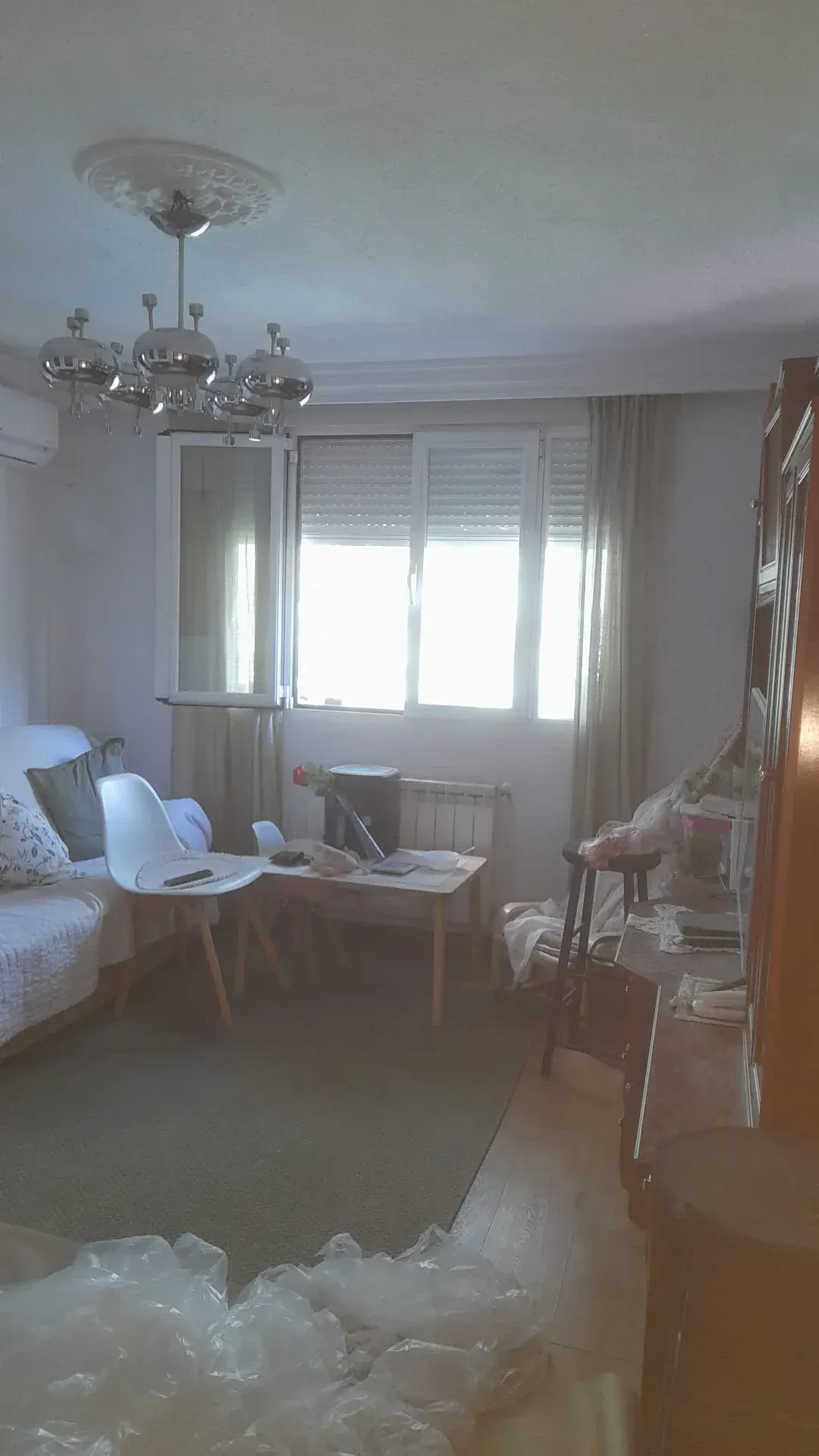 Sala de estar luminosa con sofá, sillones, lámpara de araña y luz natural que entra por las ventanas.