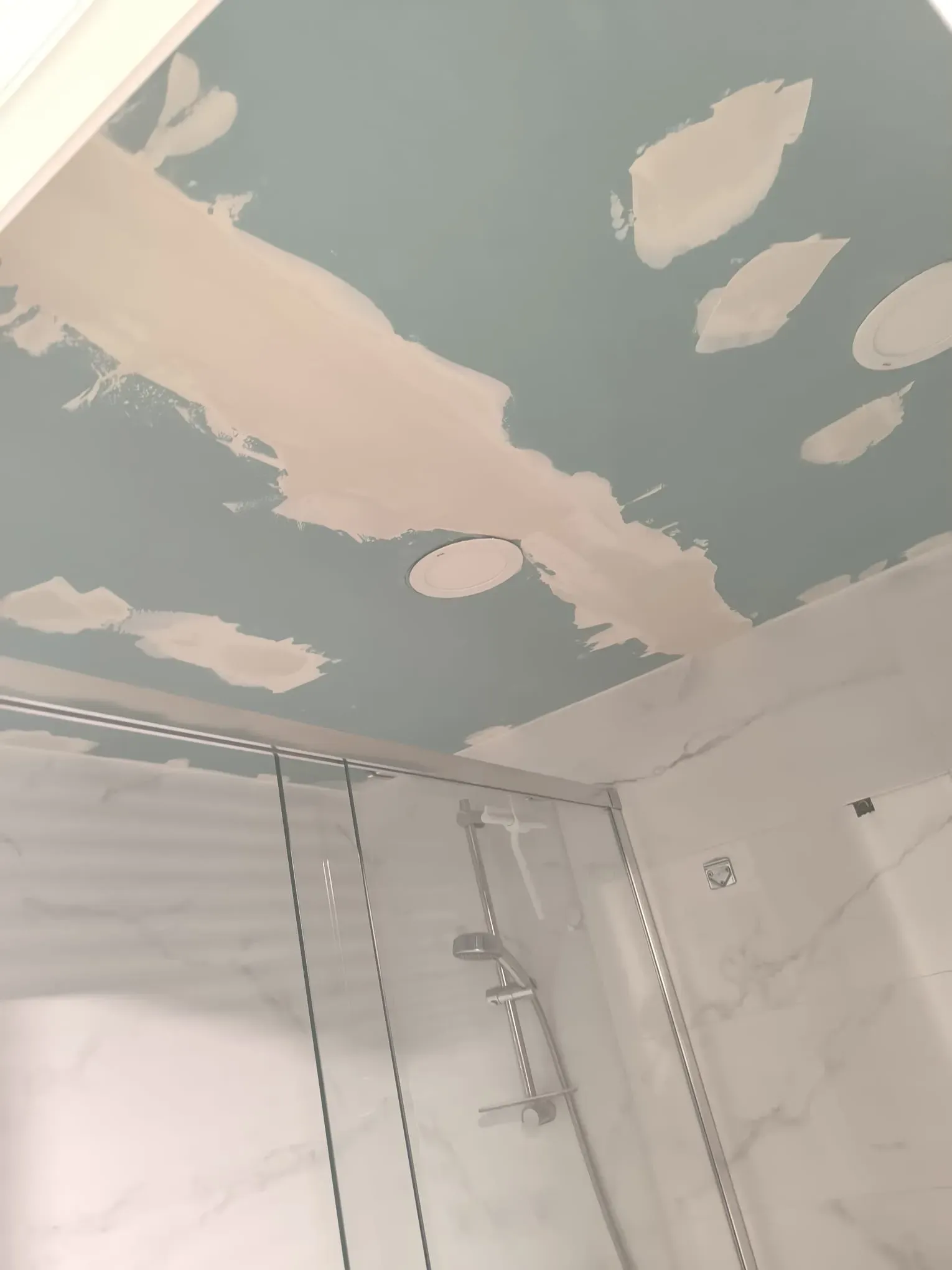 Techo del baño parcialmente pintado con parches beige y una cortina de ducha debajo.