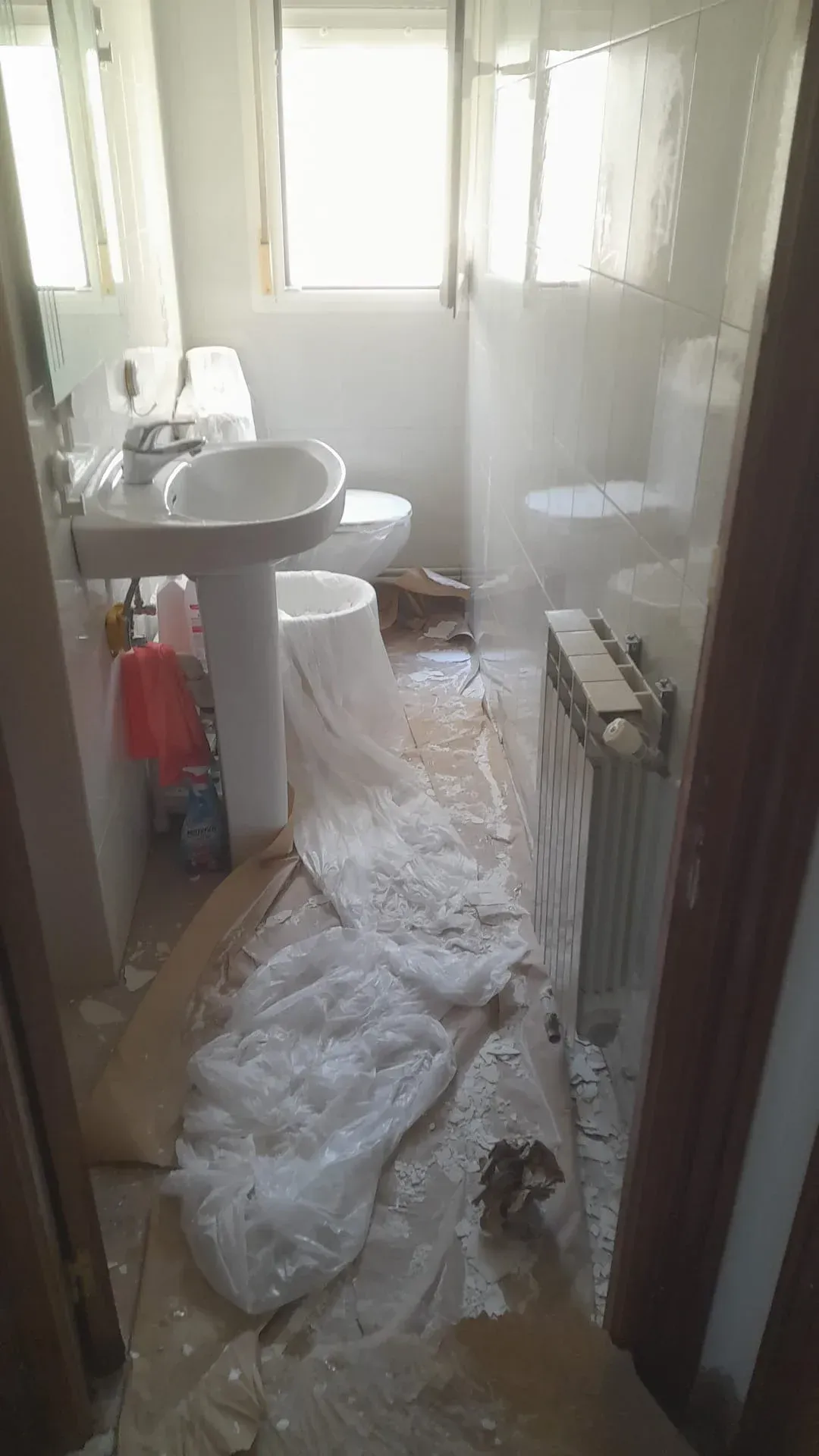 Pasillo estrecho con escombros y una sábana blanca rota en el suelo cerca de un lavabo